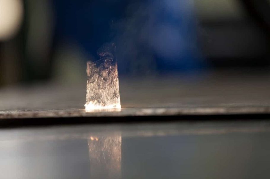 Ein metallischer Block mit einer dünnen Dampf- oder Rauchschicht darüber, vom Laser angeleuchtet.